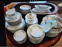 Full set of floral china arranged in stacked piles on tray and table showing plates, bowls, cups, and serving pieces.