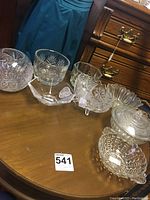 Various glass dishes and bowls arranged on a wooden surface, showing multiple shapes and decorative cut glass patterns