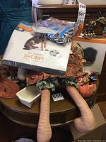 Overall Halloween lot showing the doll with striped legs, pet costume box, pumpkin container, and other decorations on a wooden surface
