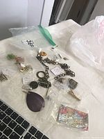 Photo showing various jewelry pieces laid out, including a purple stone pendant, metal chains, and pins with tags