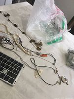 Long view of several necklaces on a white surface next to a laptop keyboard, showing a faux pearl necklace, linked metal necklace with round pendants, and more chain necklaces with different pendants
