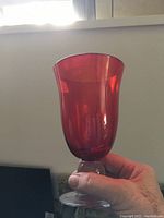 Close-up view of one ruby red glass held in hand showing its shape and color.