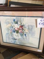 Framed print featuring white tulips in a vase with soft blue and pink tones, matted and framed with visible glazing.