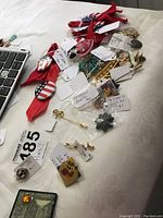 Overview of mixed pins laid out on fabric with tags and ribbons visible, showing variety and condition of items.