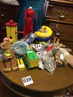 Wide shot of lot items on wooden table showing assortment of plush toys, dolls, toy trucks, and colorful toys