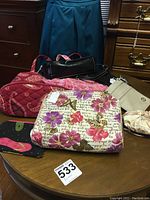 Collection of small purses displayed on a table, including a floral patterned purse, red quilted purse, black rectangular purse, pink purse, and a beige pouch.