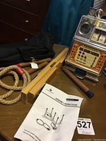 Wooden ring toss game components including three wooden poles, three rope rings, and fabric carrying case next to mini slot machine