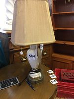 Full view of ceramic table lamp with beige shade and cord wrapped at base. Lamp stands on round ornate base, body shows rose floral design and gold highlights.