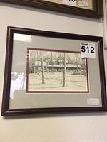 Front view of framed pen and ink winter scene drawing showing tree trunks and a building in the background, double matted inside a dark wood frame.