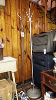 Photo of two coat racks, wooden on left and metal on right, placed against wooden wall near luggage and furniture.