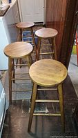 Four wooden bar stools arranged in a kitchen/basement area showcasing their height and finish.