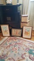 Full view of three framed Asian art prints arranged on floor in front of black cabinet next to three nested boxes.