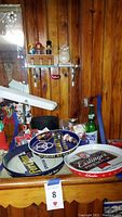 Photo showing beer advertising trays, matchbooks, and other bar items on a wooden surface near wood-paneled wall.