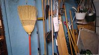 Photo of brooms, shovels, hanging plant baskets, garden tools, and garden hoses in a garage setting