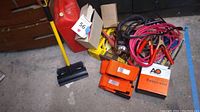 Wide shot showing multiple items on the floor including red gas can, jumper cables, orange straps, broom, and various boxes.