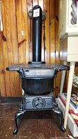 Front view of black cast iron pot belly stove with bulbous body, front air intake wheel and curved legs