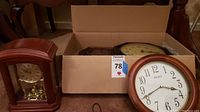 Box containing three clocks including a Bulova mantle clock with pendulum, a Seiko wall clock, and a Hamilton pendulum wall clock.