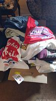 Box filled with folded clothing items including sweatshirts and jeans, showing stack of mixed colors and logos.