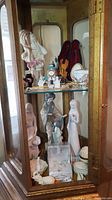 Glass cabinet displaying various figurines including Lenox elephant, Asian styled figurines, porcelain dishes, clock and violin figurine