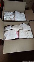 Box one showing folded white bath towels and washcloths, packed tightly.