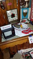 Small mini TV decoration, wooden Ortlieb's clock, Ortlieb's light-up beer sign, Ortlieb's t-shirts, and other beer memorabilia displayed on a wooden bar counter.