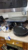 Multiple cookware items including a large stainless steel pot, stacked non-stick frying pans, metal baking sheets and a broiler tray on top.