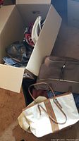Box filled with various purses including black, white, red, grey, and beige bags inside and outside the box.