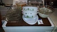 Full view of all bakeware items on surface including Pyrex casseroles with green leaf pattern, clear glass bakeware, and aluminum pans.