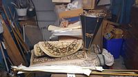 Overview of two rugs stacked with assorted curtain rods and mid-century modern umbrella stand; garage setting