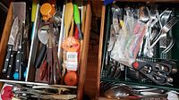 Two wooden drawers filled with assorted kitchen utensils, knives, and flatware arranged loosely. Includes metal knives, wooden spoons, scissors, and other small utensils.