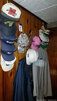 Hats hanging on a wooden rack mounted on wall showing various snapback hats and IBM long sleeve shirt hanging beneath.