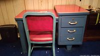 Photo showing vintage metal desk with red laminate top along with matching vinyl padded chair.