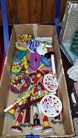 Box containing over 20 tin noisemakers and horns with colorful lithographed designs packed tightly, showing the variety in shapes and sizes.