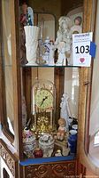 Full view of the cabinet shelf showing various figurines, vases, clock, and trinket boxes.