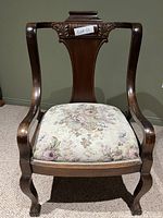 Front view showing chair's curved armrests, carved backrest, and floral seat upholstery