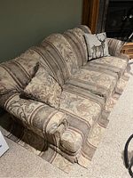 Full side view of antique cloth couch featuring patterned upholstery and decorative pillows; shows overall shape and style of the couch.