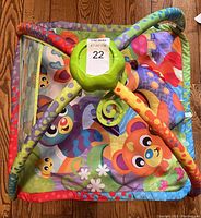 Top-down view of the colorful baby play mat showing animal illustrations and fabric arches crossing in the middle with some toys attached.
