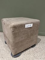 Beige square foot stool viewed from front left angle, showing fabric upholstery and label Lot 04.