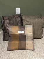 Photo of five assorted couch cushions: two brown vertical striped, one beige solid textured, one plaid in brown shades, and one more beige solid textured cushion, all showing signs of use and needing cleaning.
