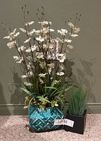 Full view of two potted artificial plants, one large floral arrangement and one small green grass-like plant