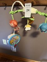 Full view of the baby mobile attached and hanging, includes hanging animal toys, music unit, and remote.