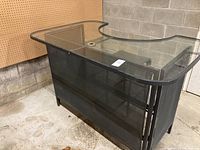 Full view of the patio bar showing glass top and black metal mesh frame, positioned against a concrete wall.