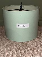 Turquoise cylindrical lamp shade resting on carpet floor, labeled Lot 50.