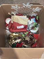 Overview of mixed Christmas decoration box contents including mugs, bowls, stockings, centrepieces, garland, and snowflake ornaments.