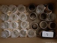 Top down view showing 24 glass jars in total, arranged in rows, some wrapped with lace and tied with raffia bows and others plain or painted.