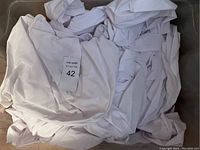 White cloth pieces wrinkled and folded inside a bin, with a label showing the lot number.