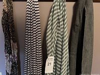 Four women's scarves hanging on a rack in different patterns and colors, including stripes and floral.