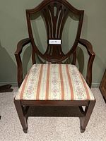 Front view of antique cherry wood chair showing shield backrest, armrests, and striped upholstered seat