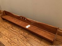 Side view of long wooden shelf showing the flat base, raised edges, and heart-shaped cutouts on back panel.