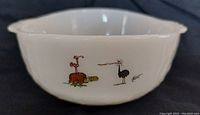 Side view of white Fire King milk glass bowl featuring colorful Hart cartoon characters printed on surface.